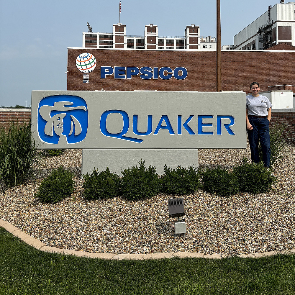 Harmony standing near a large sign that says Quaker on it.