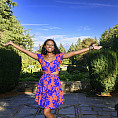 Damaris posing outside with both of her arms raised and Mount Hood in the background. She is wearing a colorful purple and blue dress.