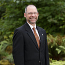 Eric smiling outside wearing a suit and orange tie.
