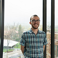 Drew smiling at the camera, wearing a short sleeve checkered shirt.