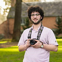 Nadav smiling outside wearing a white shirt and glasses.