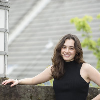 Annika, wearing a black sleeveless top, smiling while standing in front of a concrete wall outside The Dovecote.