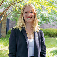 Helen smiling outside wearing glasses and a dark blazer over a white shirt.