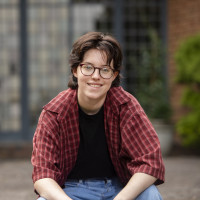Apollo smiling outside, wearing a red plaid shirt over a black t-shirt.