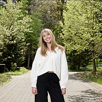 Grace posing outside in a white top and black pants.