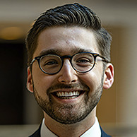 Alex smiling at the camera, wearing glasses.