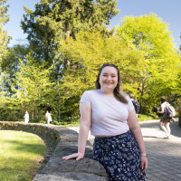 Savannah posing outside. She is wearing a light colored tshirt and floral skirt.