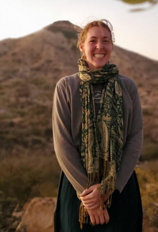 Bijou smiling outside, wearing a long-sleeve shirt and a scarf.