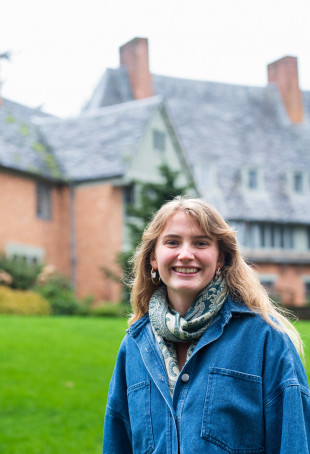 Beau posing in front of the Manor House, wearing a blue jacket and scarf.