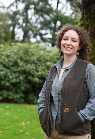 Izz posing outside wearing a brown vest over a button-up shirt.