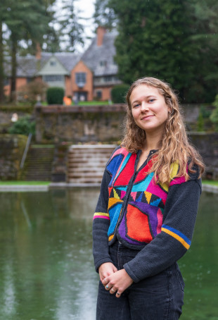 Elsa posing in front of Manor House and reflecting pool, wearing a colorful jacket.