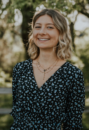 Nicole, smiling, standing in front of trees on a sunny day. Processed with VSCO with j2 preset. Student-supplied profile photo due to COV...