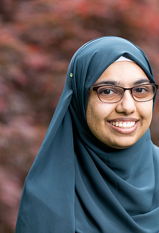 Nuzhat smiling at the camera, wearing glasses and a blue hijab.