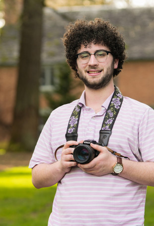 Nadav smiling outside wearing a white shirt and glasses.