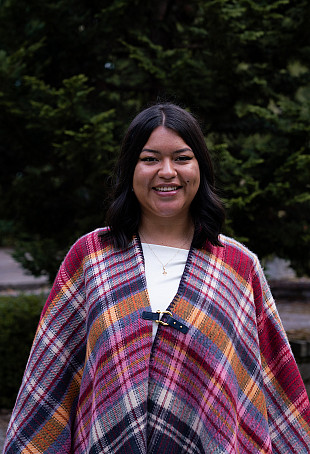 Gaby posing outside wearing a colorful plaid cape.