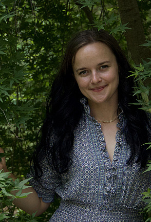 Hanna posing outside in some green foliage. She is wearing a blue patterned dress.
