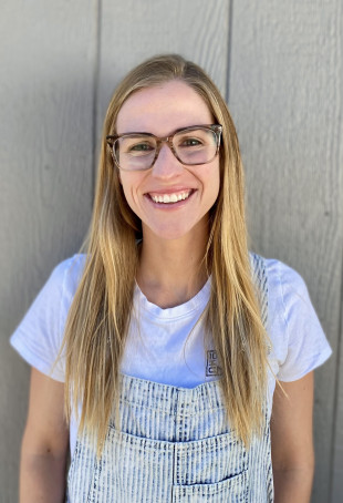 Headshot of Jessye Lavine BA '16. She is a light skinned female with long straight blonde hair, standing in front of a gray wall, wear...