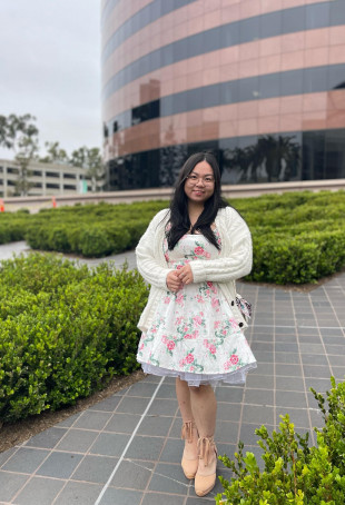 Jessica posing outside, wearing a white dress with pink flowers on it and a white cardigan.