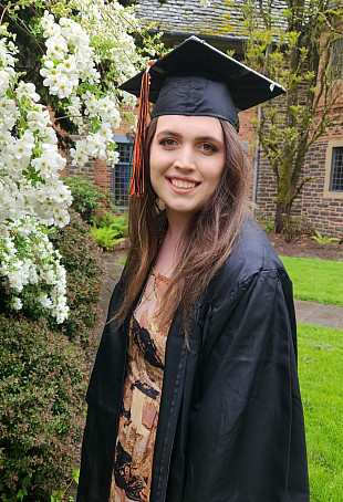 Isabella posing outside wearing her graduation cap and gown.