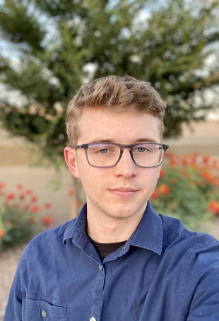 Tyler smiling outside. He is wearing glasses and a blue shirt.