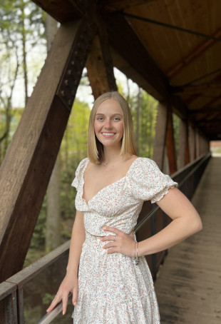 Kelsey smiling outside wearing a white dress.
