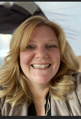 Donna smiling at the camera wearing a black shirt and tan cardigan.