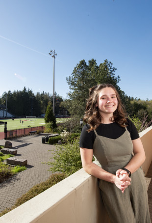 Grace posing in front of Griswold Stadium. She is wearing a black tshirt under a green jumpsuit.