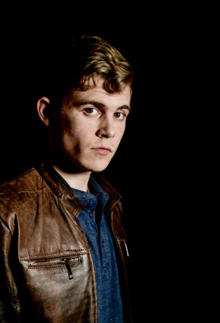 Noah looking at the camera, wearing a brown leather jacket.
