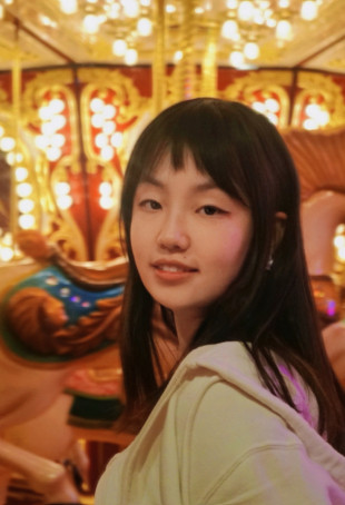 Polly smiling in front of a carousel. She is wearing a white top.