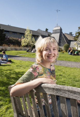 Burton, sitting on a bench outside Albany Quadrangle, wearing a floral printed top.