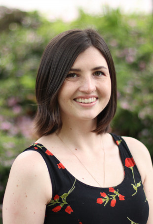 Hannah smiling outside. She is wearing a black tank top with red flowers.