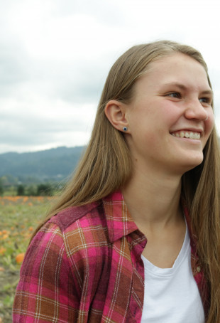 Katya smiling outside wearing a red flannel shirt over a white top.