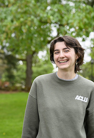 Madeleine smiling outside, wearing a sage green sweatshirt.