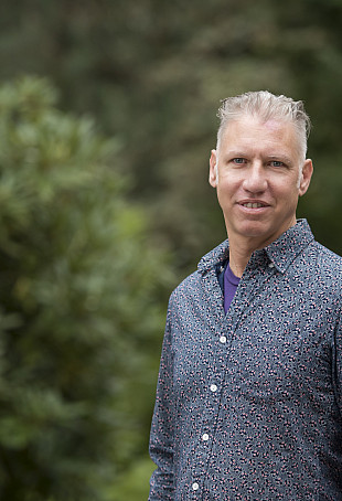 Elliott posing outside, wearing a blue button-up dress shirt.