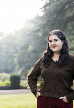 Sophia posing outside with her hands on her hips, wearing a long-sleeved brown sweater and red pants.