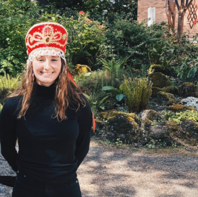 Marcella, in an elaborate red and silver Russian hat and all black outfit, smiling on a sunny day...