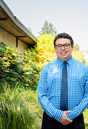 Jeremy smiling at the camera outdoors, wearing a button-up shirt and tie.