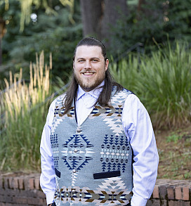 Andy smiling and posed in front of brick and forested background