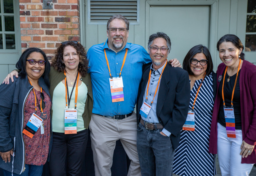 Five diverse alumni posing and smiling in front of Frank Manor House