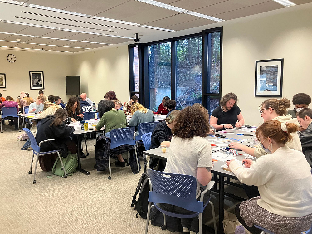 people sitting at tables in a classroom working on art projects