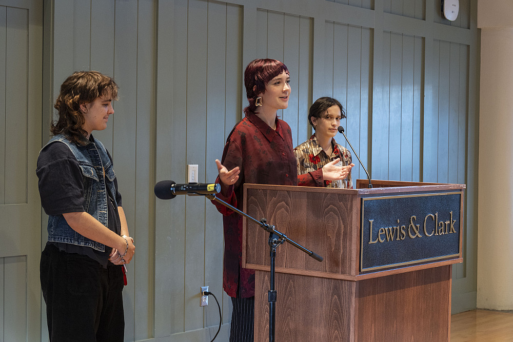 3 people standing, one at podium