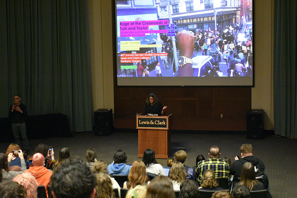 woman in front of audience at podium with image on screen behind her