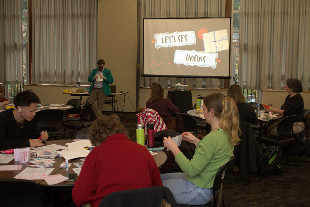 People seated at tables working with paper, guided by a person next to a screen with images.