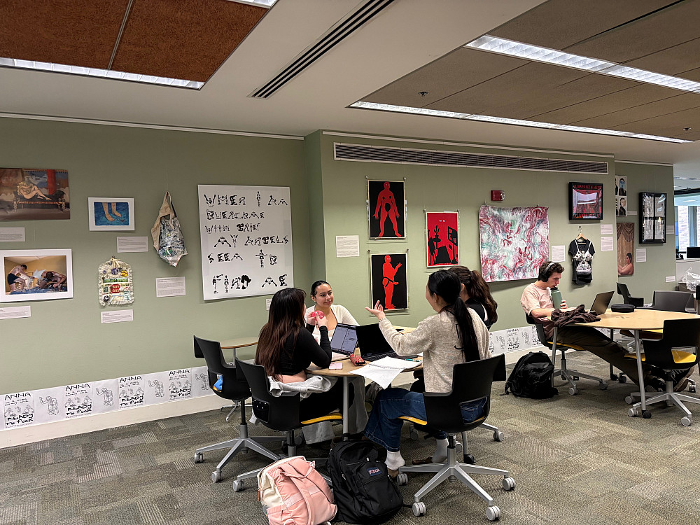 Students seated at a table next to art mounted on the wall.