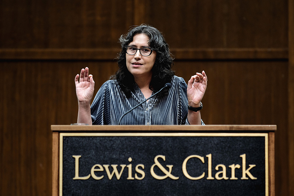 Woman with hands raised at podium that says Lewis & Clark.