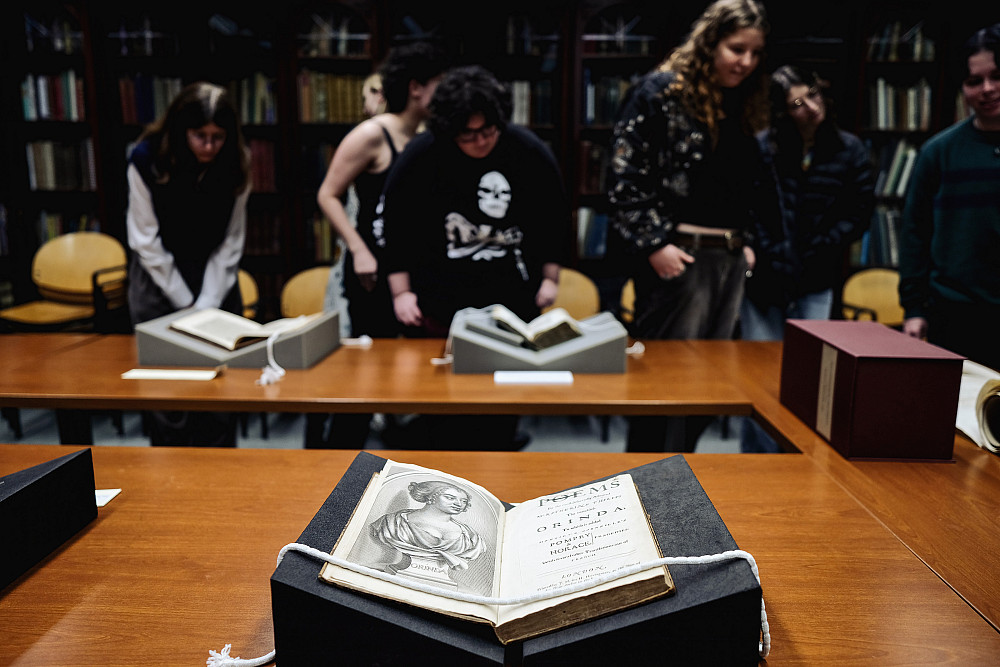 A rare book display in the foreground, and students observing other books in the background.