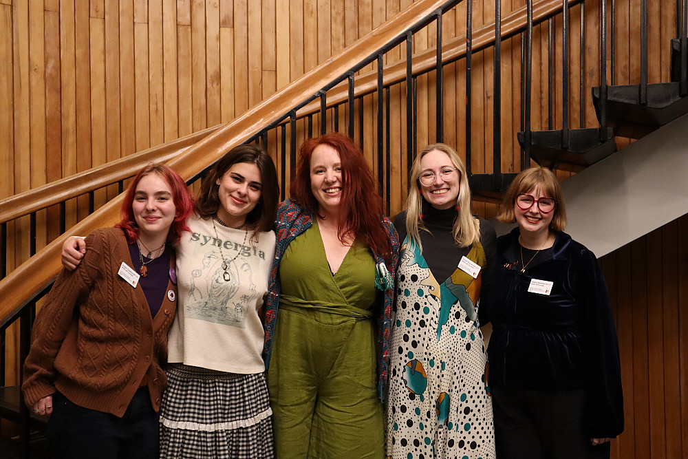 5 women posing arm-in-arm in front of a staircase.