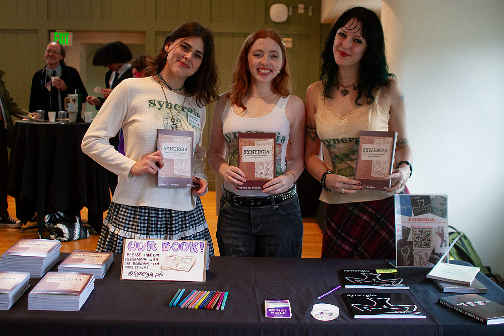 Three females standing together holding a copy of the same book.