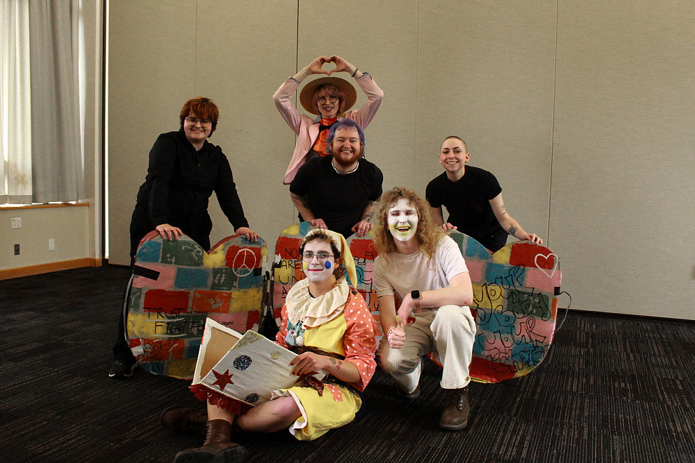2 people in made up as clowns, seated, and 4 people behind them posing with various props.