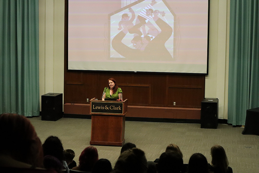 A woman standing at a poidum in front of a large screen.
